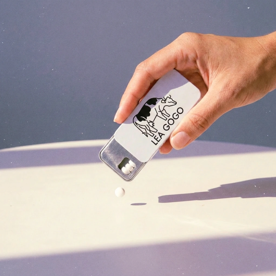 Lea Gogo high-strength lactase enzyme tablets placed on a mauve background with some lactase pills falling from the tin.